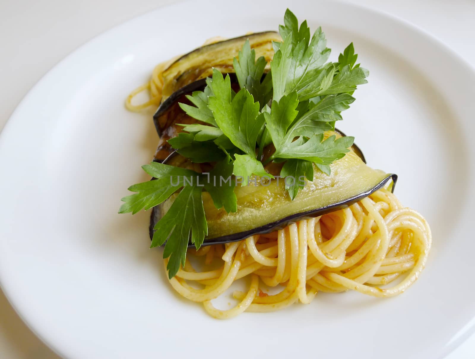 Traditional Italian cuisine. Close up of spaghetti roll with aubergine, fresh tomatoes sauce and parsley.