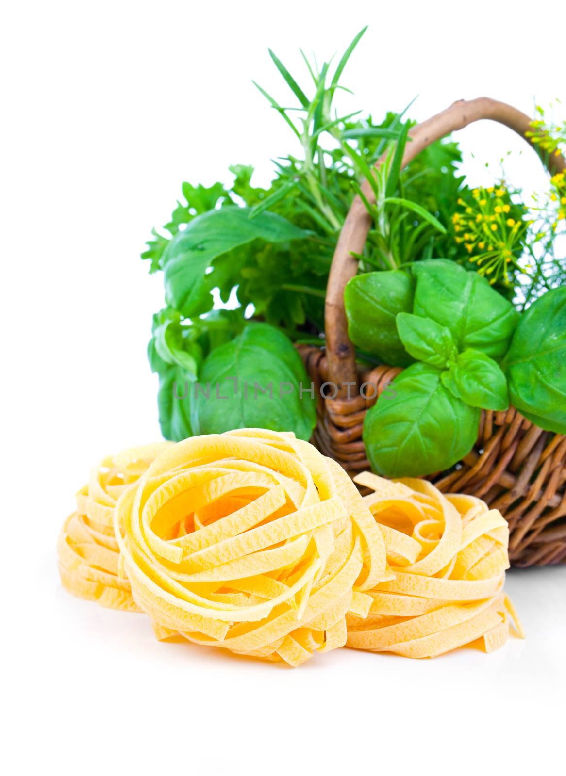 Italian pasta fettuccine nest with wicker basket green herbs, on white background