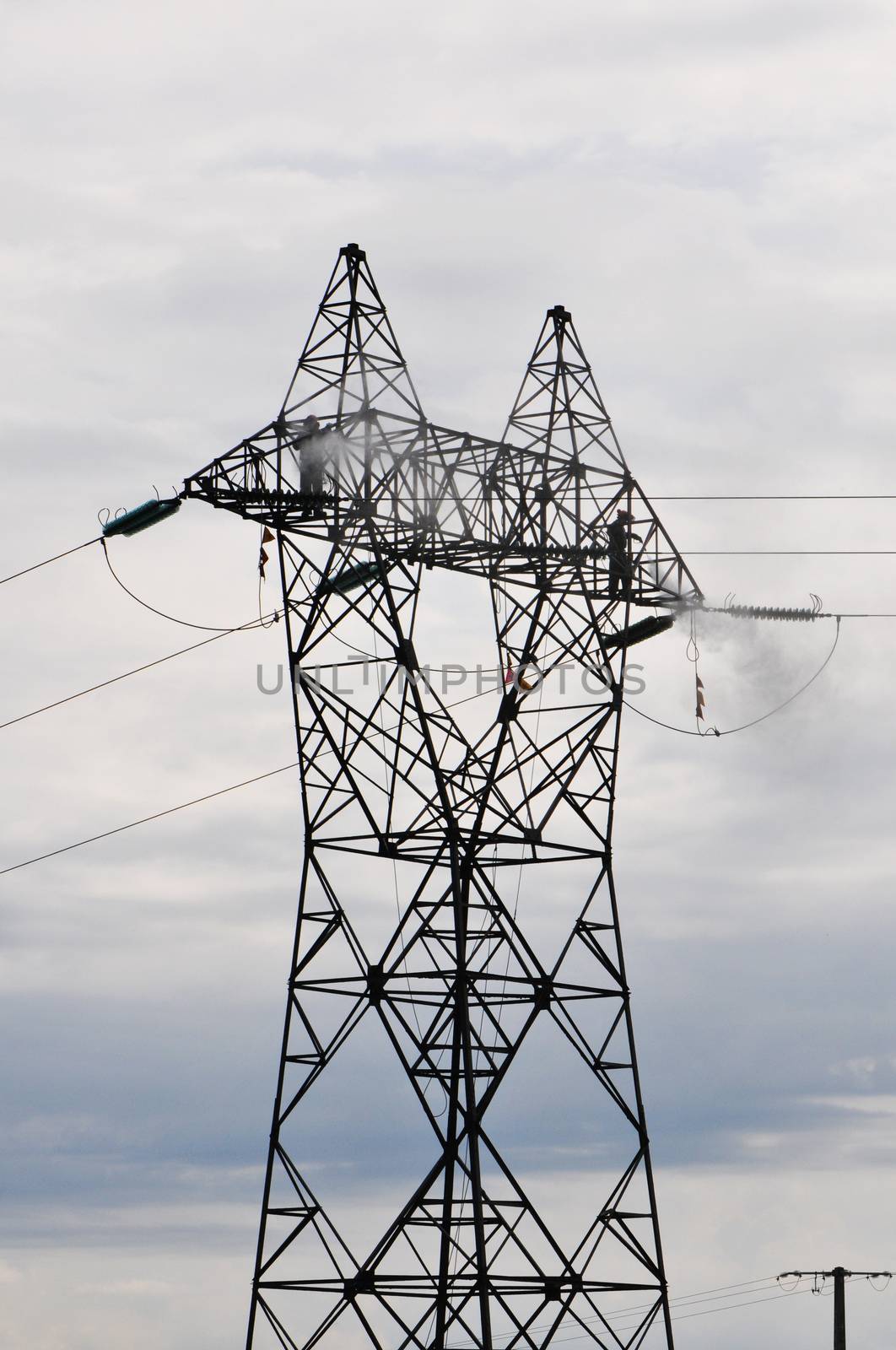 Two Guys Cleaning Big Electrical Pylon with a Cloudy Sky