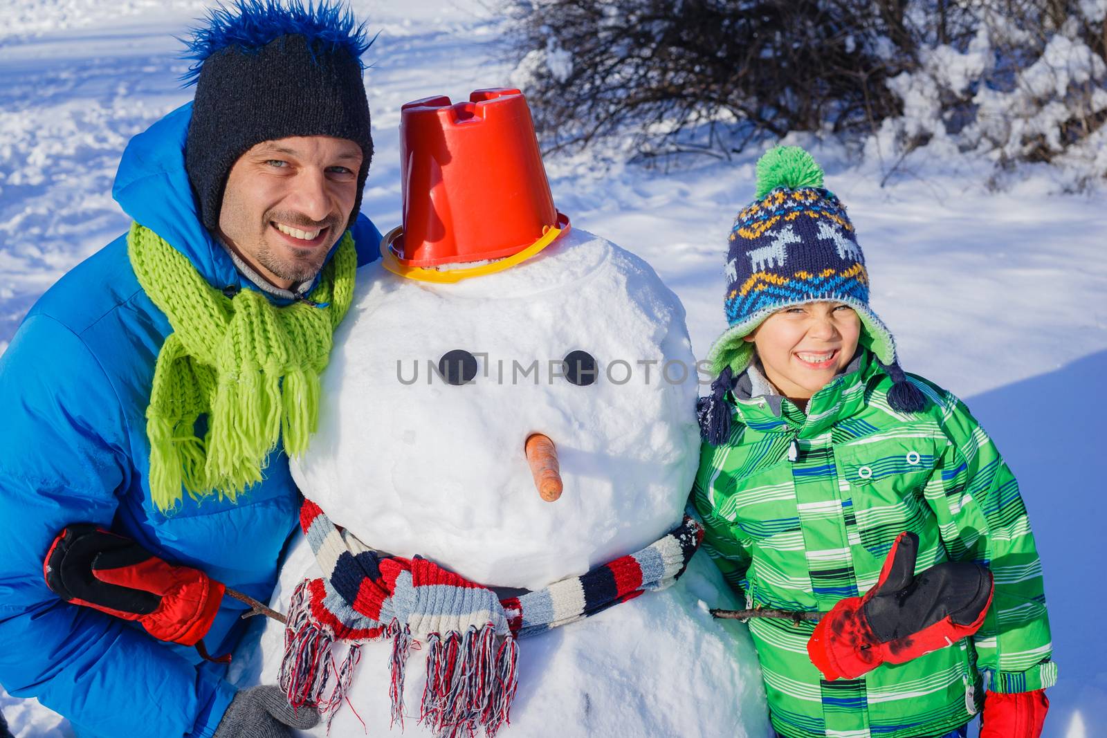 Happy liitle boy with his father building snowman outside in winter time