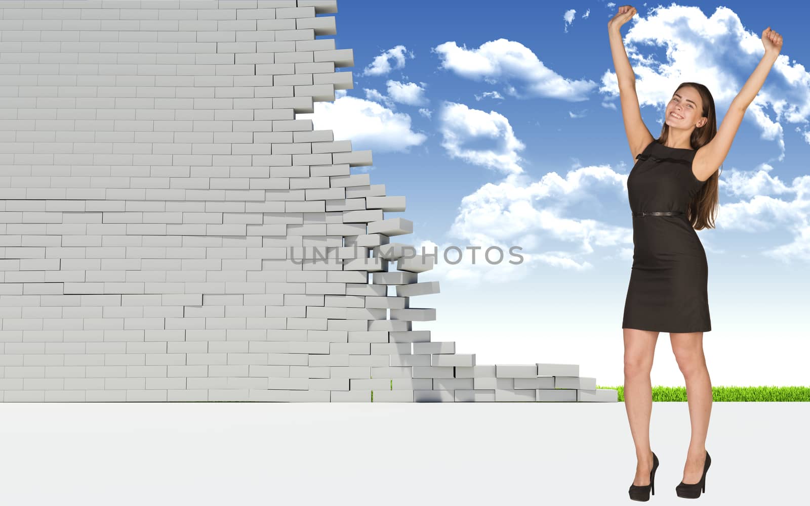 Beautiful businesswoman in dress happily raised his hands up, looking at camera. Dilapidated brick wall, green meadow and sky as backdrop. Concept of freedom