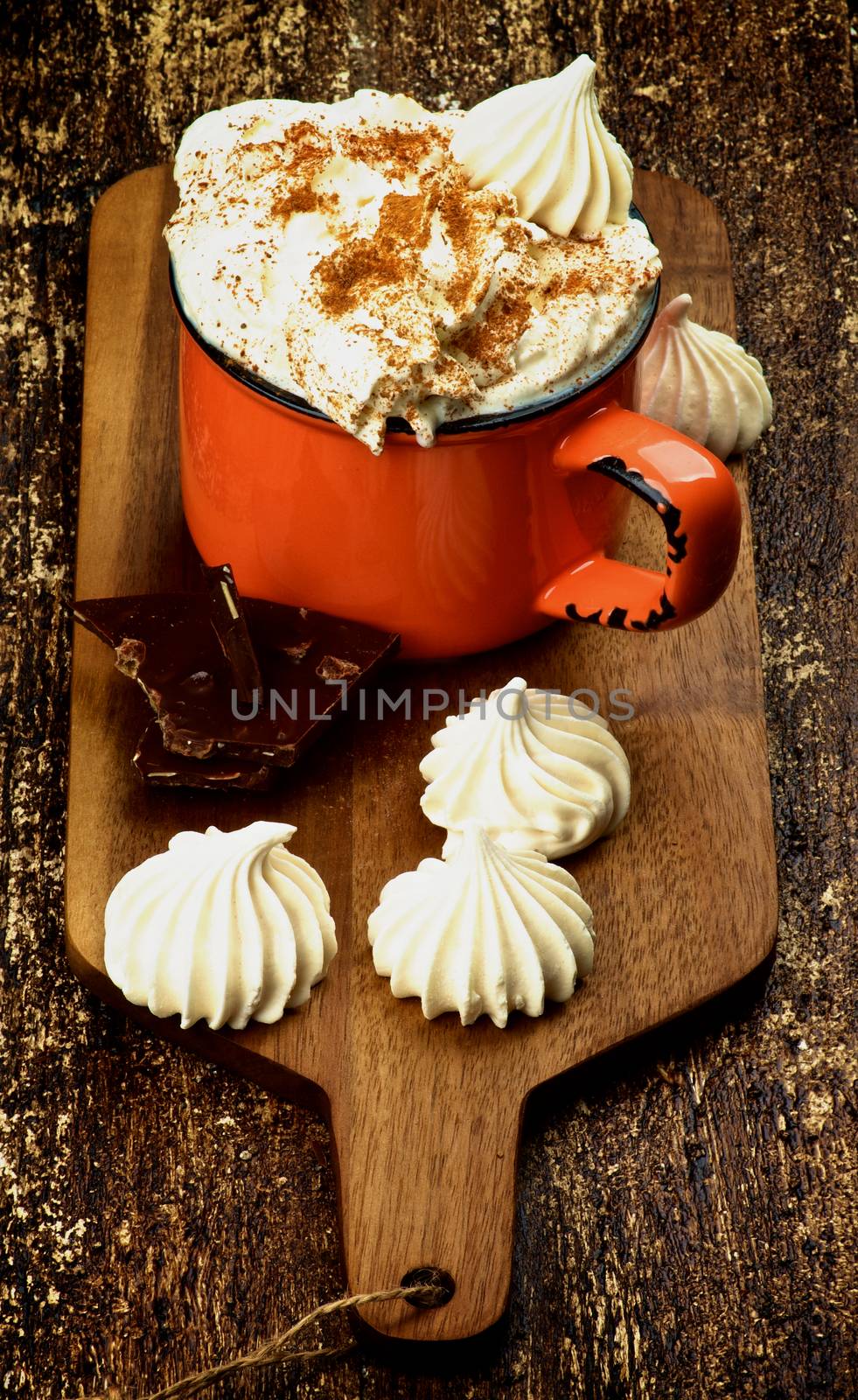 Arrangement of Hot Chocolate in Orange Cup Whipped Cream and Cinnamon, Meringues and Dark Chocolate on Cutting Board on Rustic Wooden background