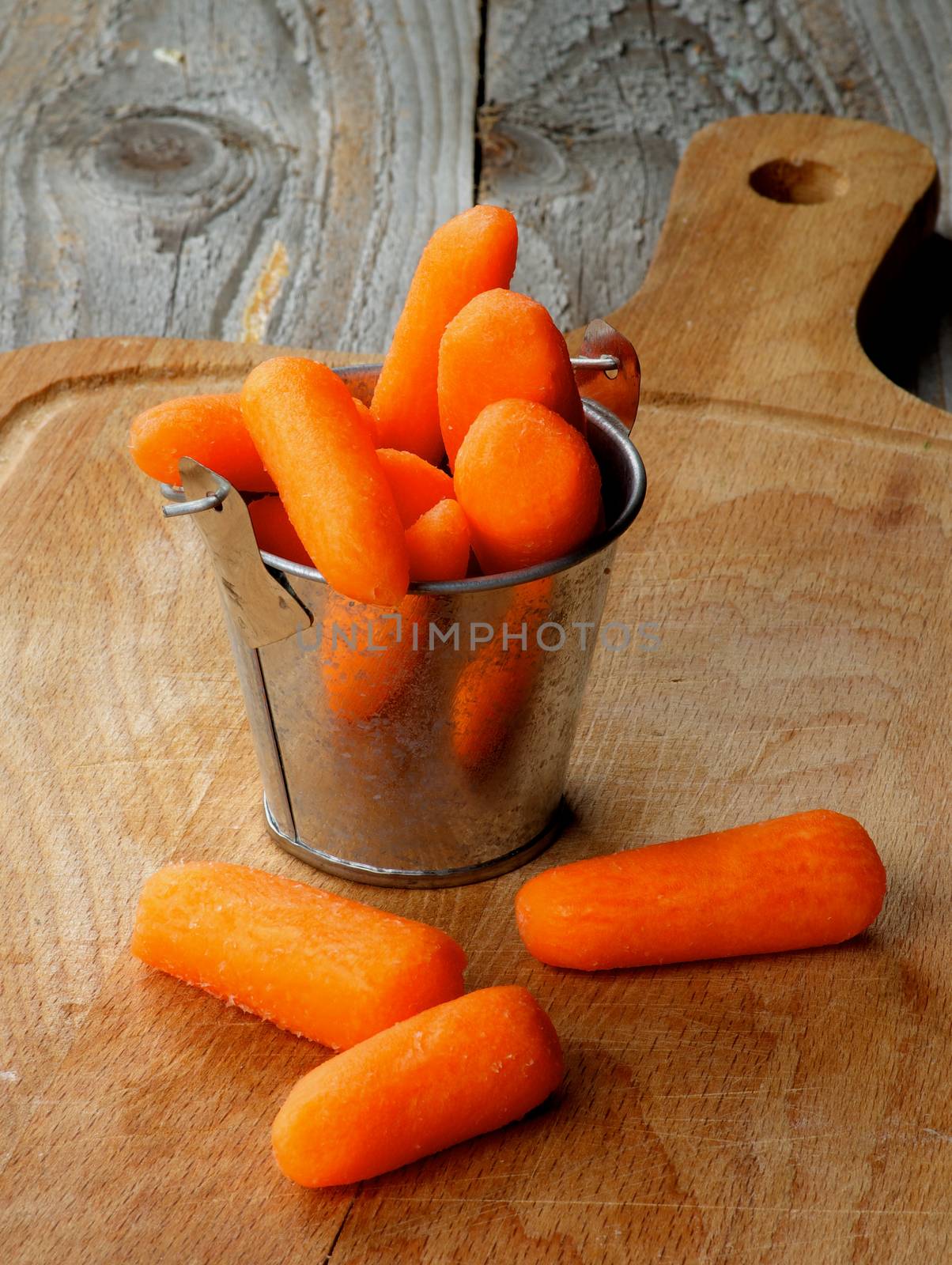 Heap of Fresh Raw Peeled Baby Carrots in Tin Bucket closeup on Wooden Cutting Board