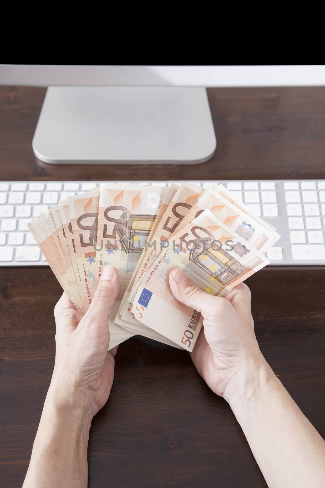 woman hands counting fifty Euros banknotes over keyboard computer brown wooden table