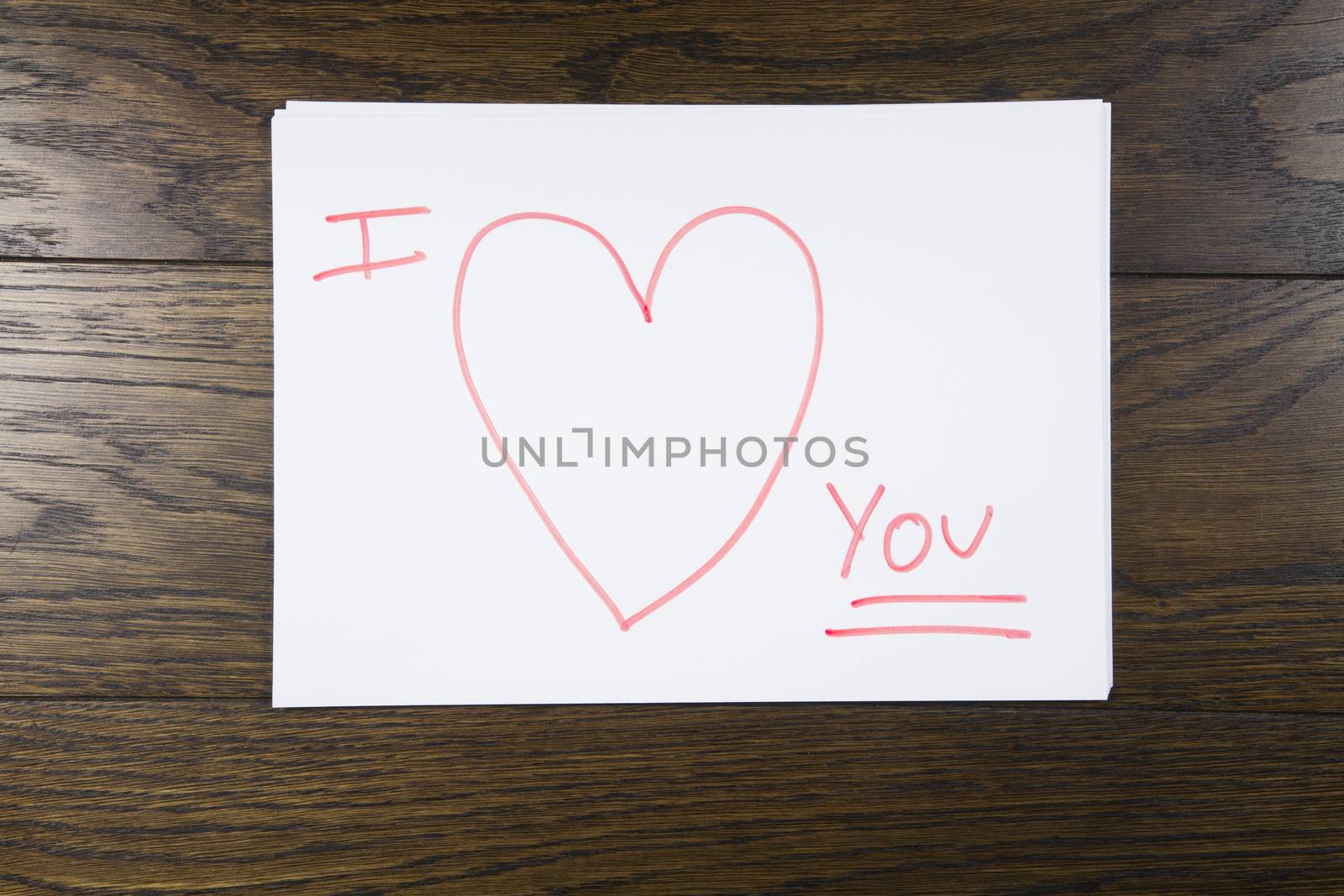 I love you text written with orange marker on white paper over brown wooden background