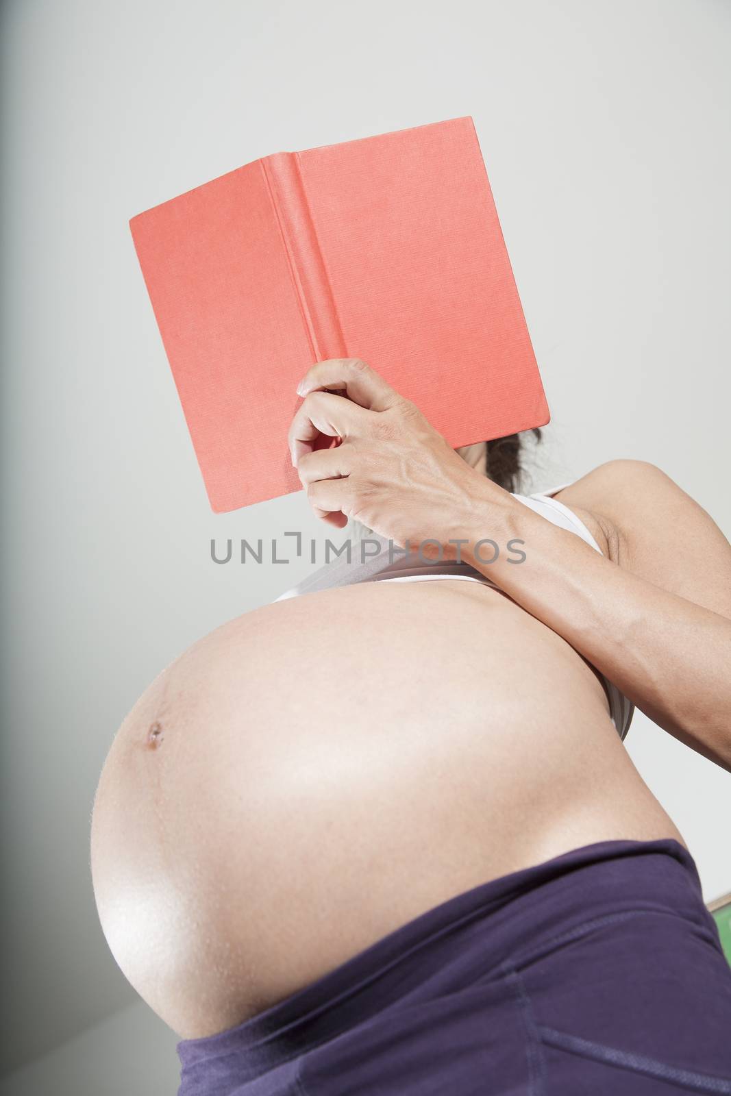 pregnant woman purple trousers bare belly stand reading a red book