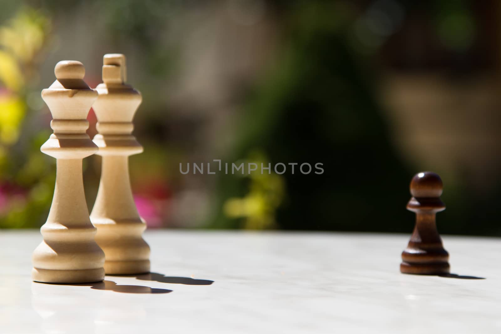 Chess pieces, pawn and queens on white table with blurry background.