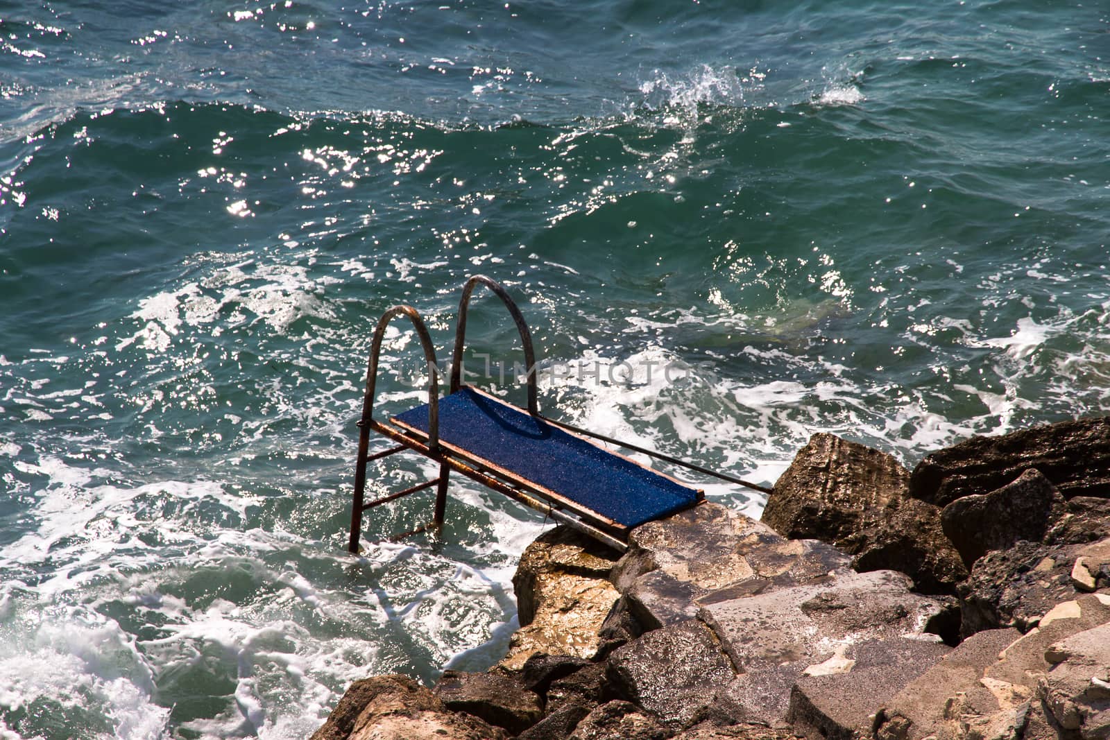 Pier on wavy sea and beach with stones.