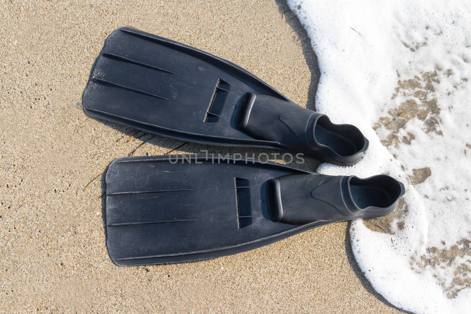 Black plastic flippers on sea sand and wavy sea with foam.