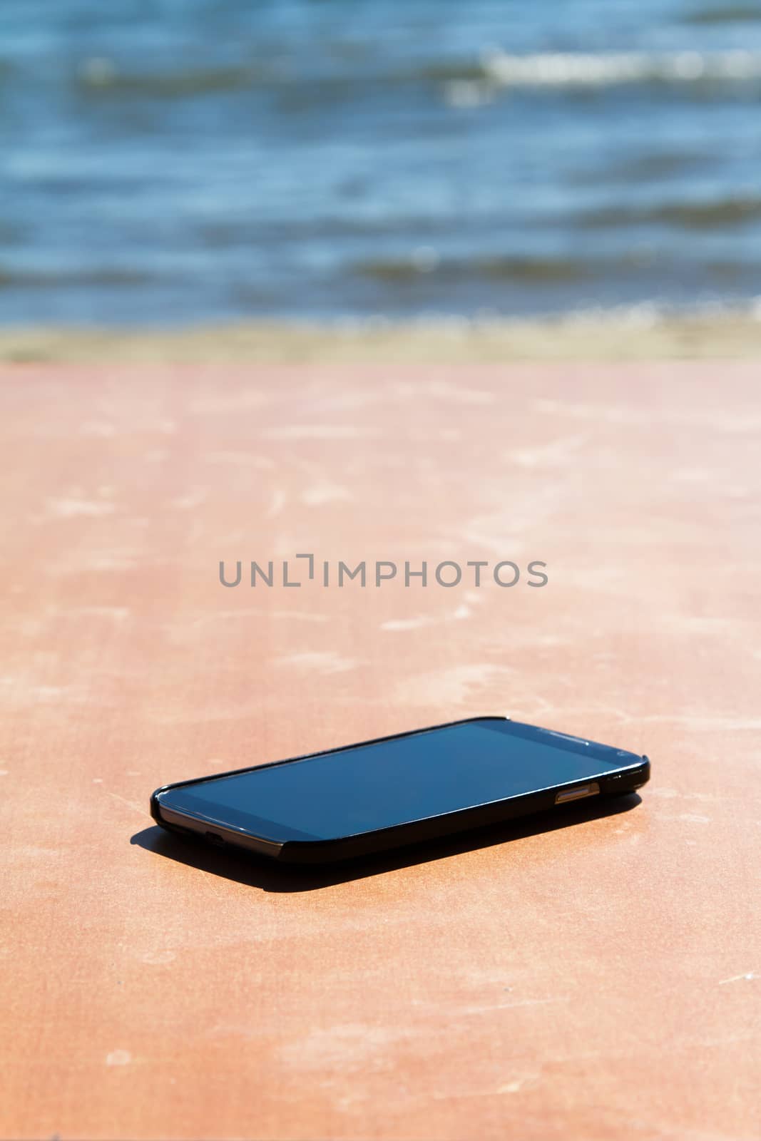 Smart phone on wooden table, wavy sea on blurry background.