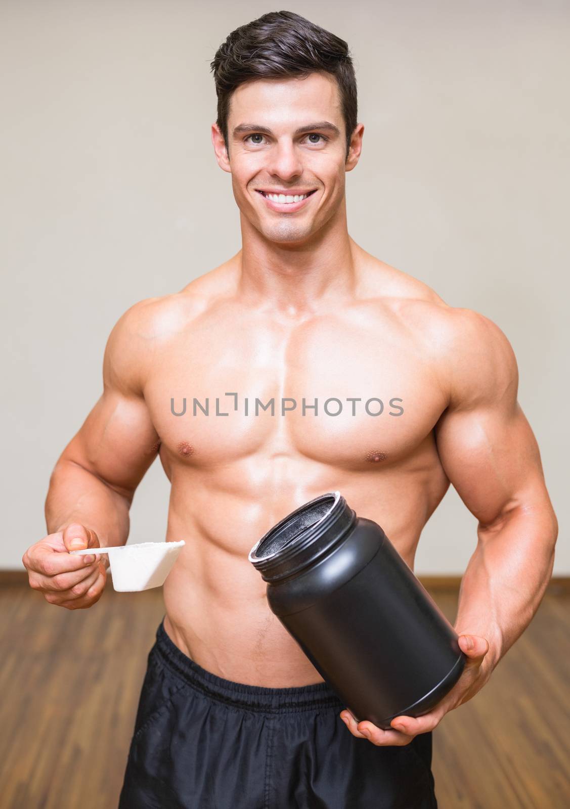 Body builder holding a scoop of protein mix in gym by Wavebreakmedia