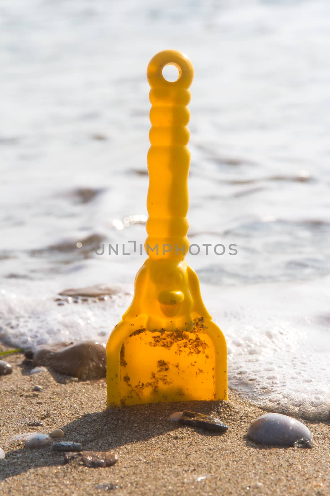 Yellow toy scoop standing on sand near sea with foam.