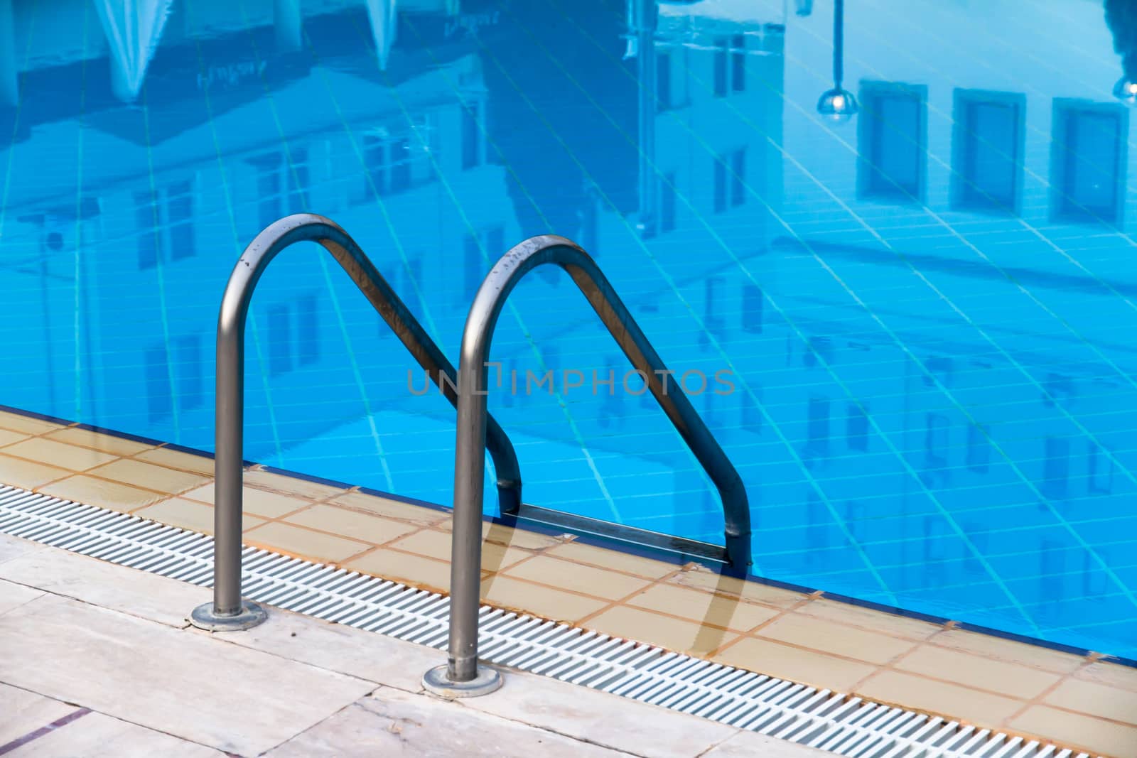 Close up of stair at blue swimming pool with reflection of the hotel.