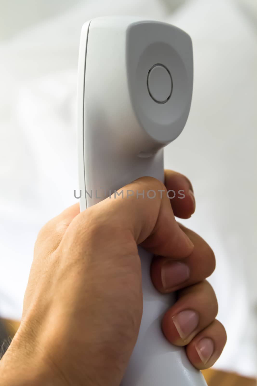 Hand holding white telephone tube in hotel room.