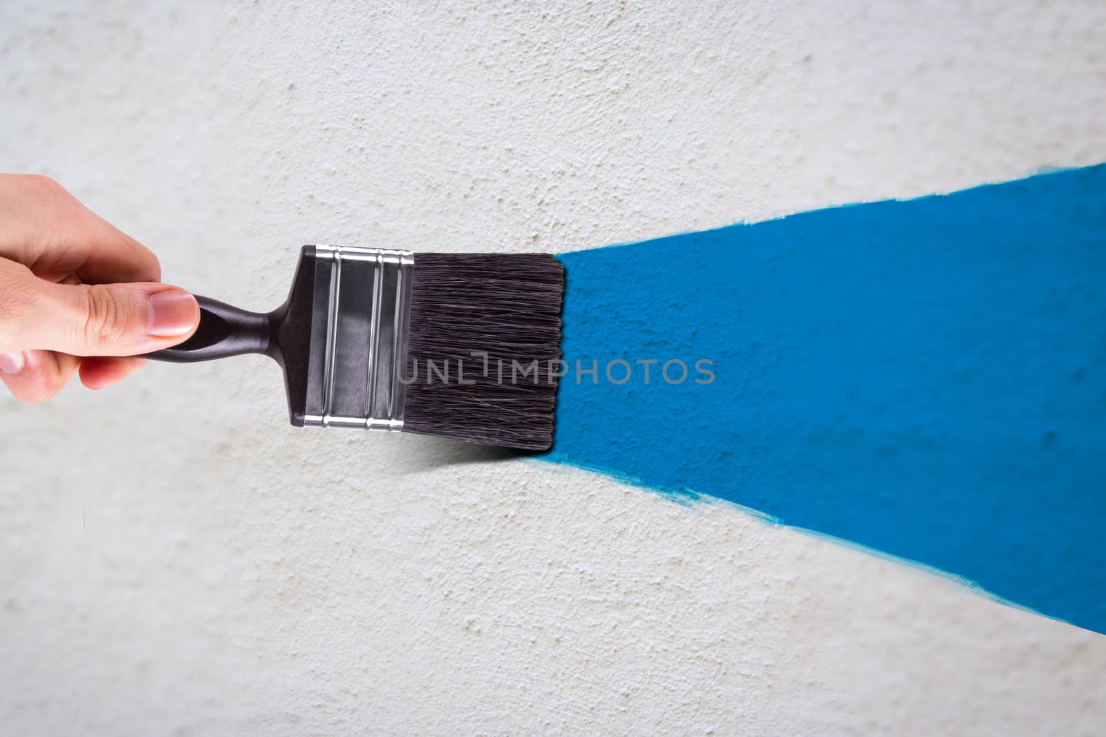 Male hand holding paint brush and painting white wall with blue color.