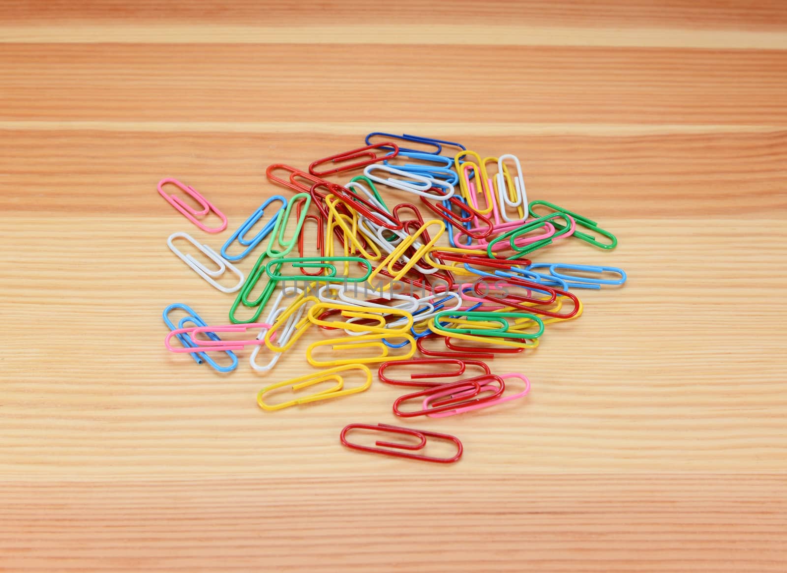 Pile of small coloured paper clips on a wooden background