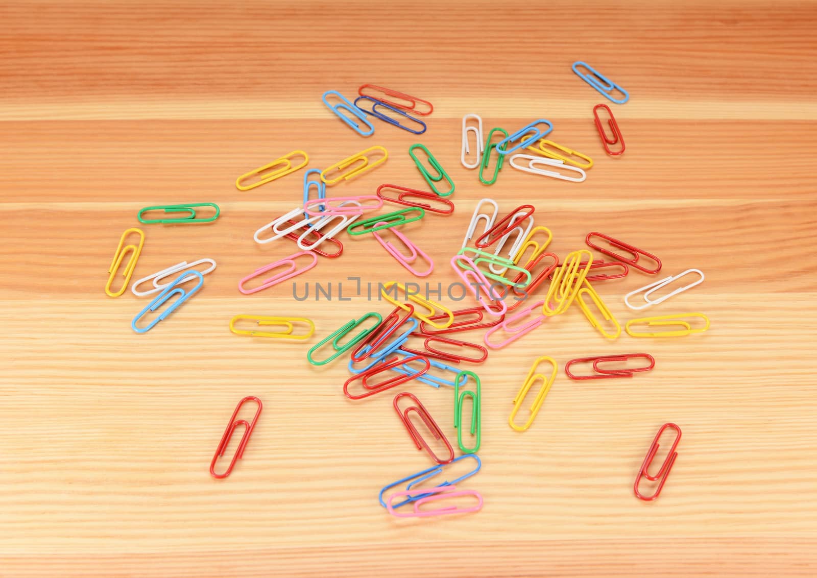Multi-coloured paper clips scattered across a wooden background