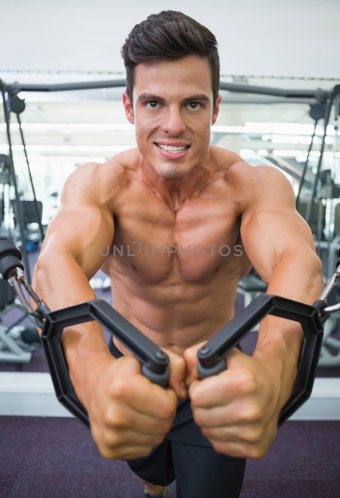 Portrait of a shirtless young muscular man using resistance band in gym