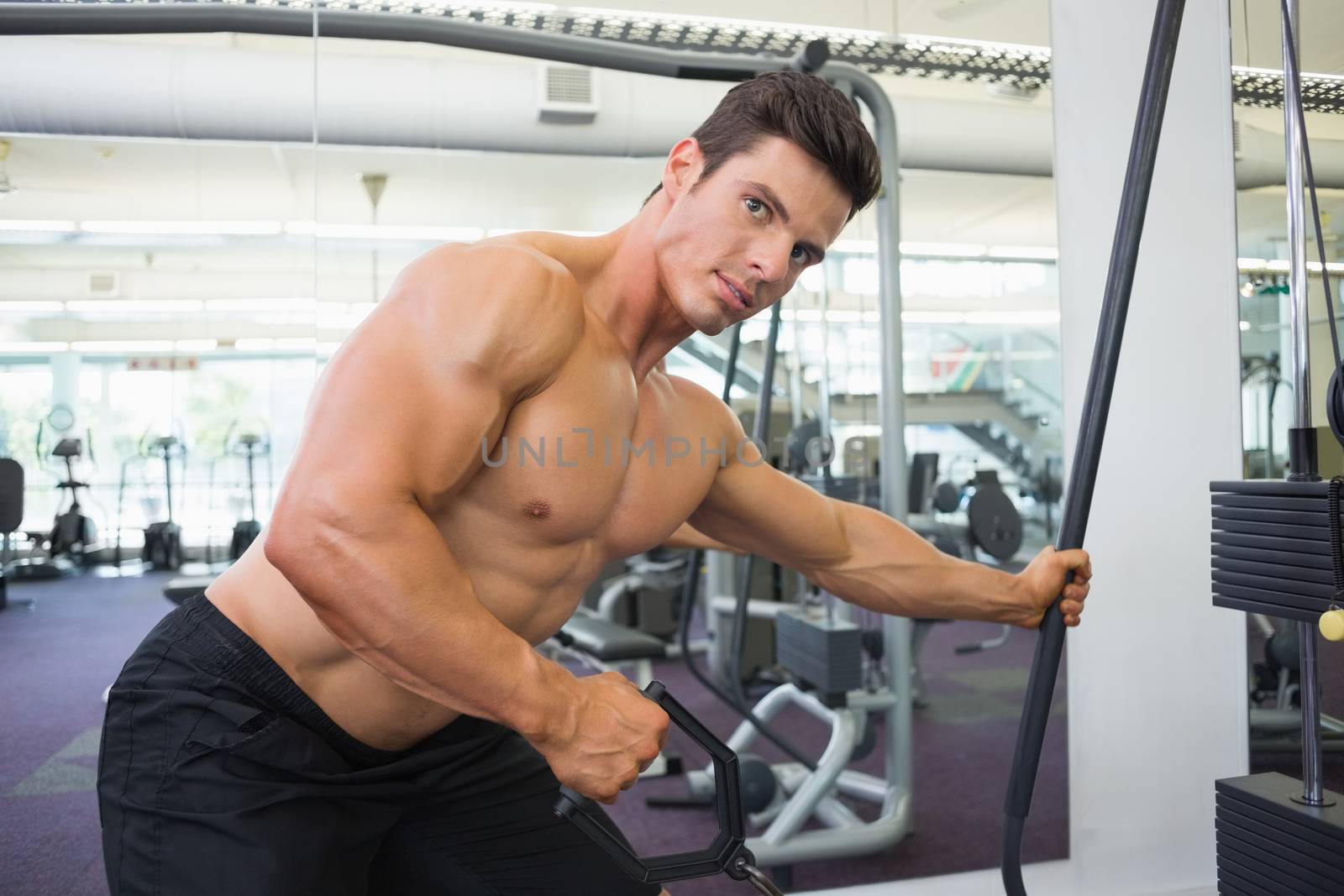 Side view of a shirtless young muscular man using resistance band in gym