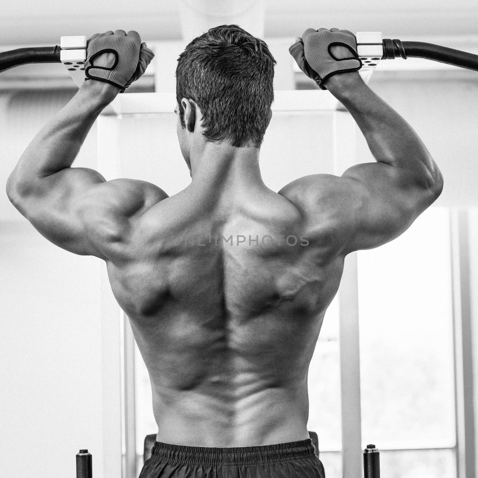 Rear view of a male body builder doing pull ups at the gym