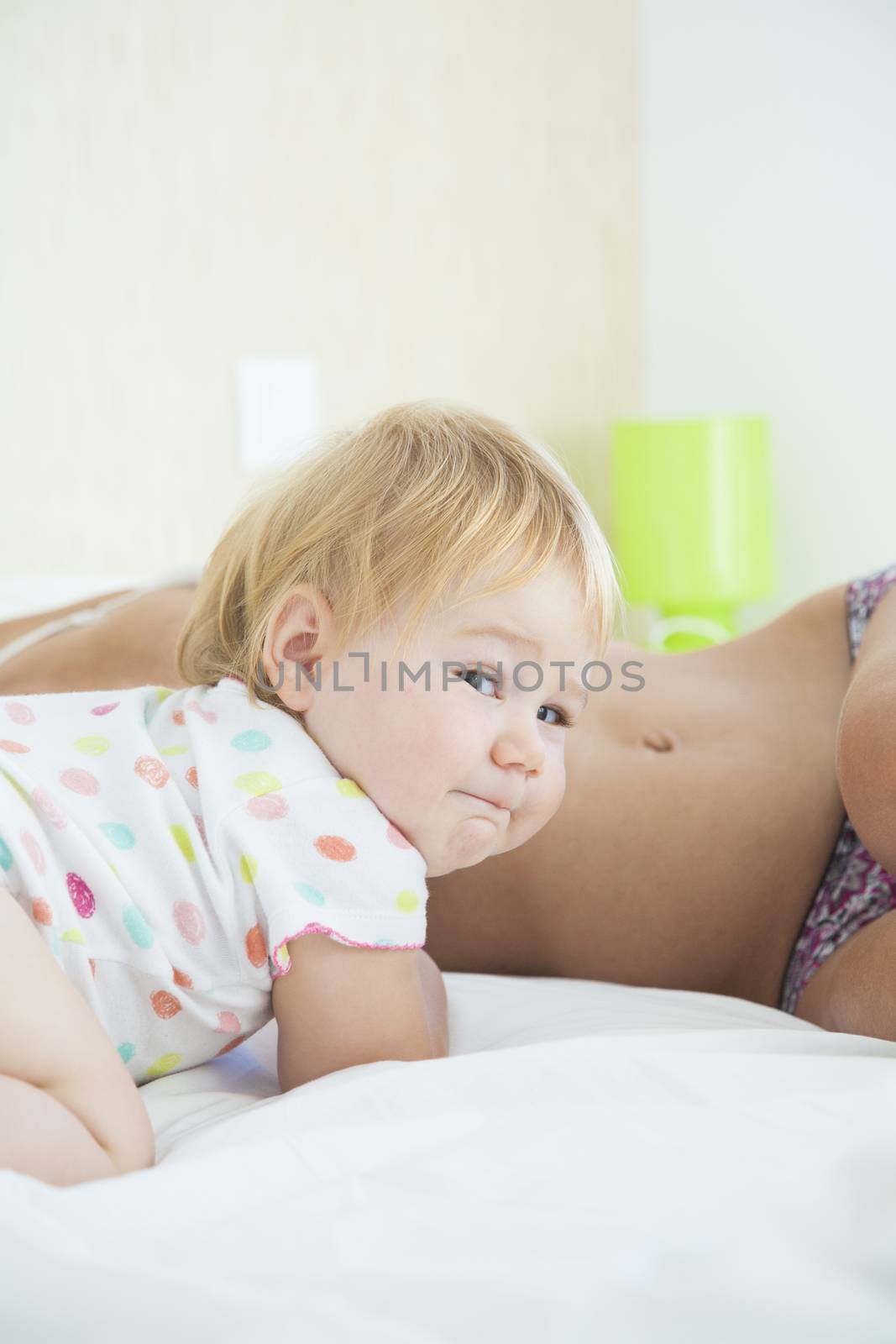 one year baby face looking at camera and woman mother bare lying behind on white quilt bed