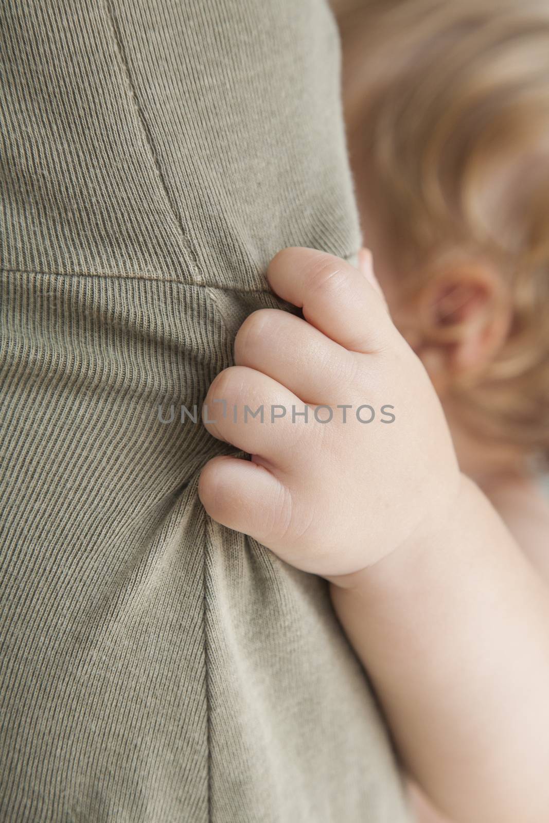 closeup one year blonde baby hand holding green mom dress