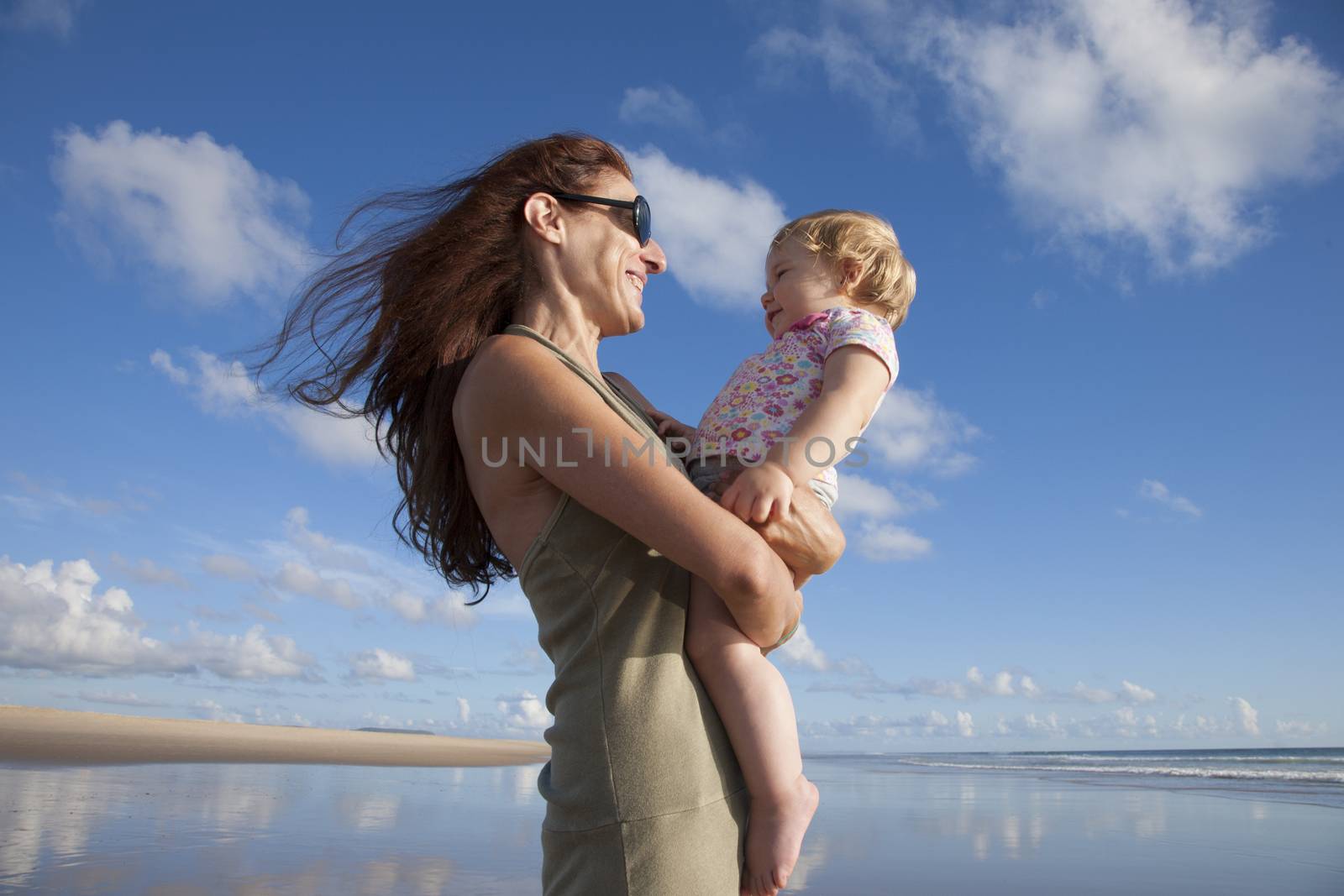 happy green dress woman with sunglasses and one year blonde baby in her arms at beach Conil Cadiz Spain