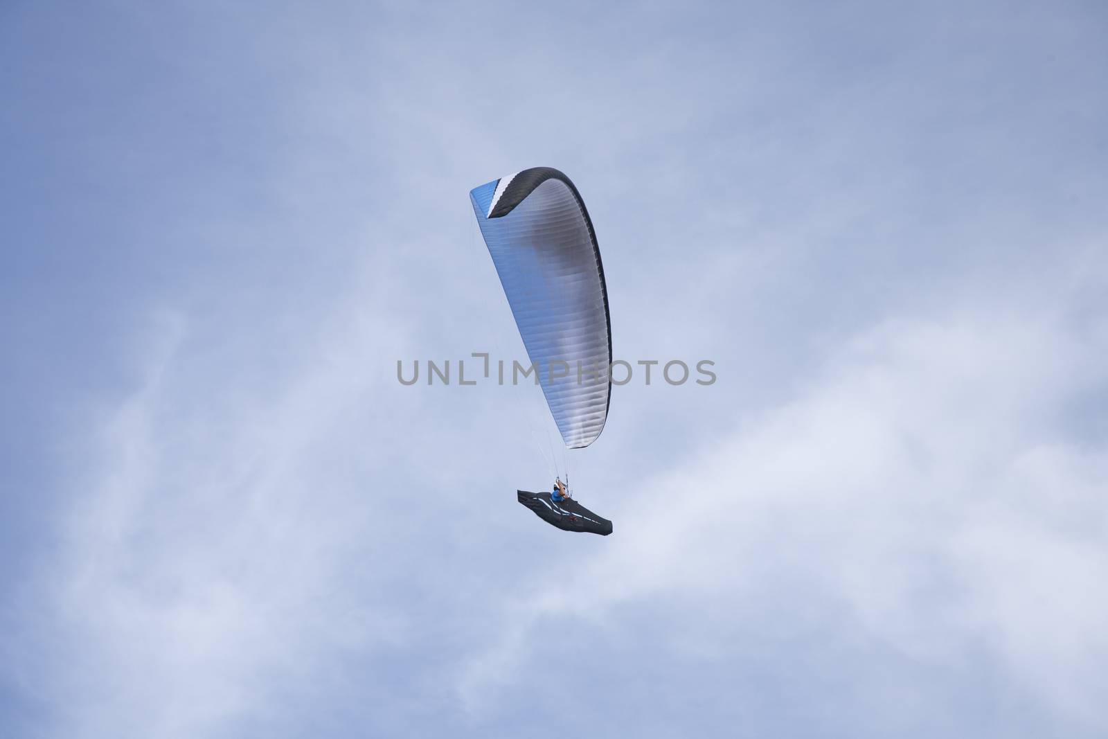 white paraglider flying in cloudy white and blue sky