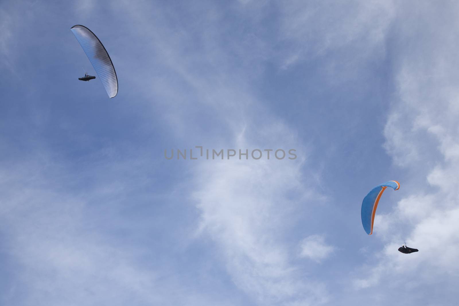 white and blue paragliders flying symmetric in cloudy white and blue sky