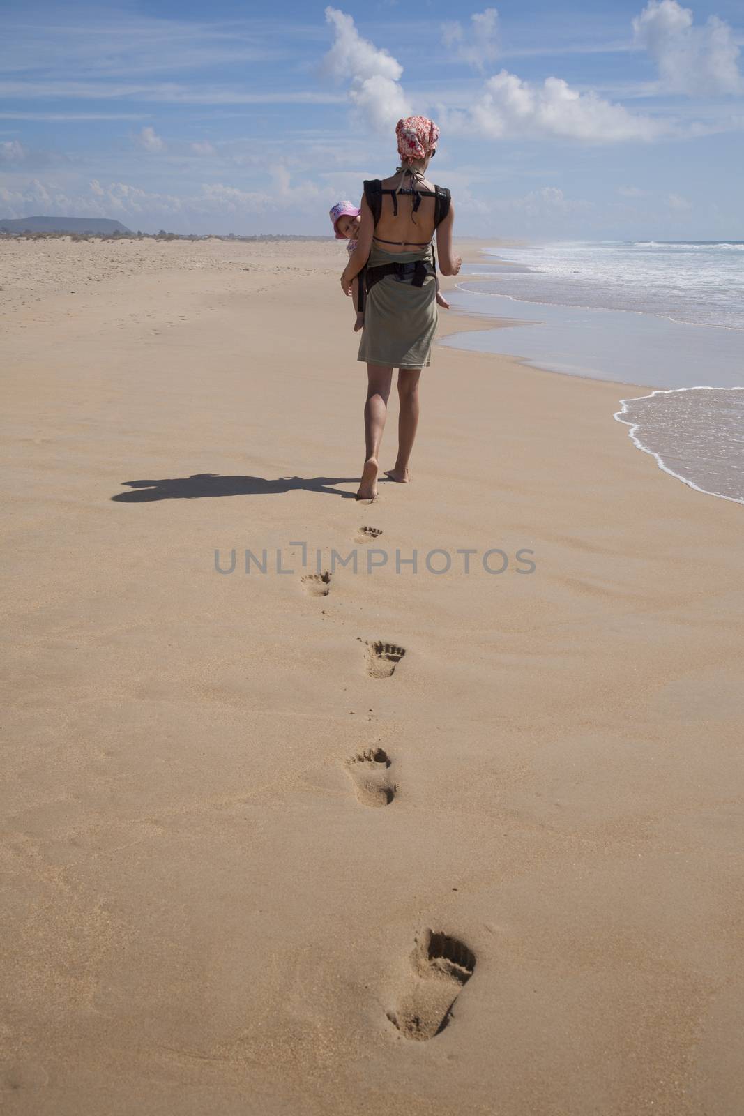 back woman mother with headscarf green dress carrying her one year baby in front rucksack walking beach next to Conil Cadiz Andalusia Spain