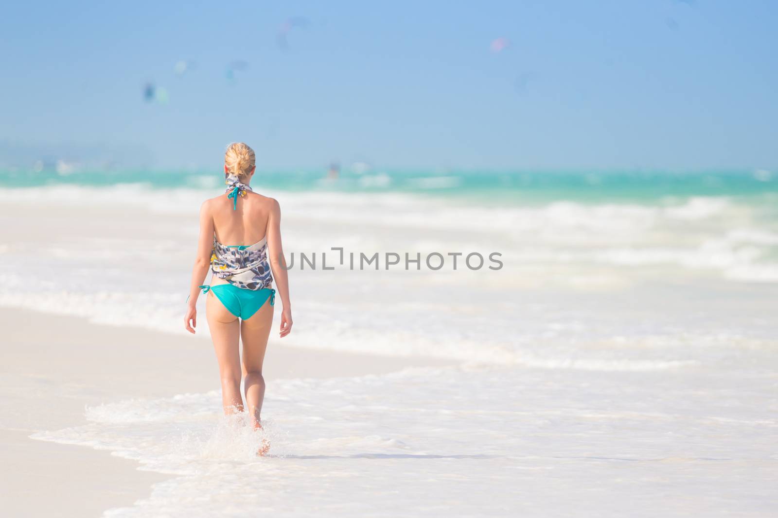 Happy woman having fun, enjoying summer, walking joyfully on tropical beach. Beautiful caucasian model  wearing colorful scarf and turquoise bikini on vacations on Paje beach, Zanzibar, Tanzania