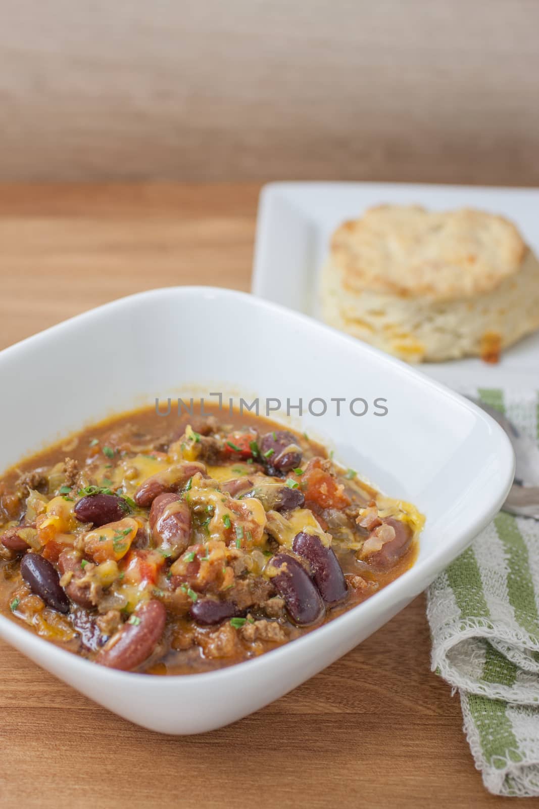 Fresh homemade chili in a white bowl with a homemade cheddar and garlic biscuit on side.