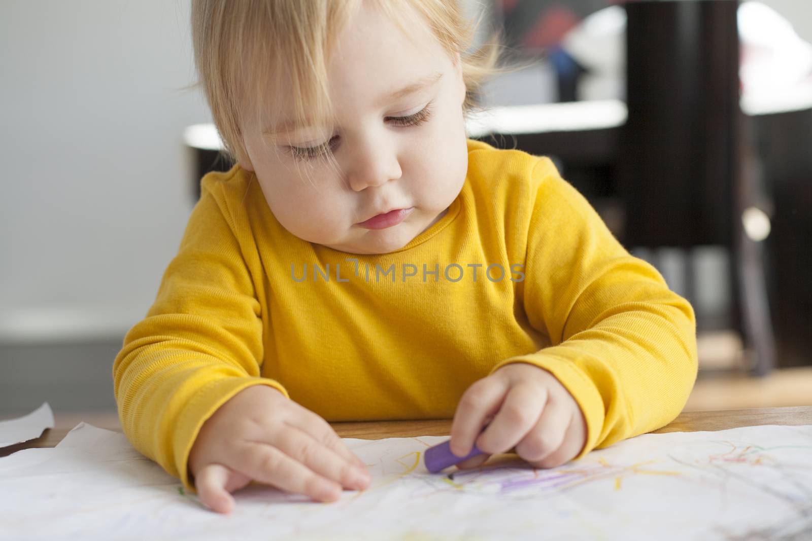 blonde sixteen month baby yellow sweater painting white sheet paper on table inside home