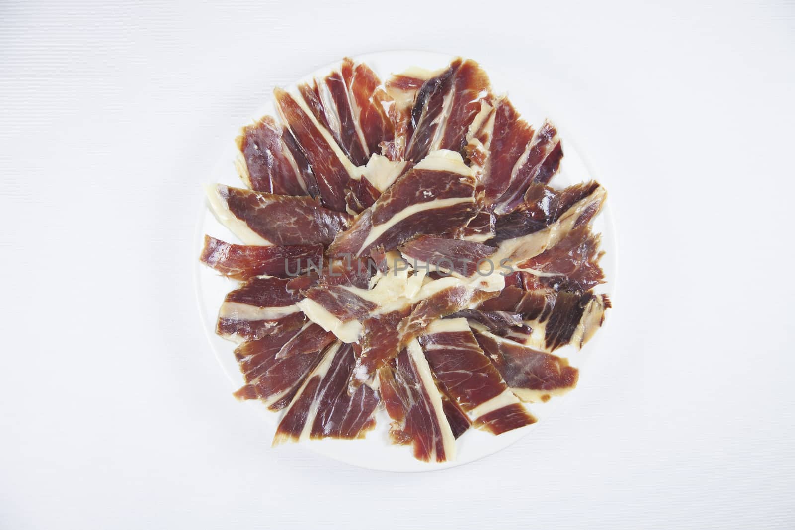 pile of typical spanish iberico ham sliced on white dish