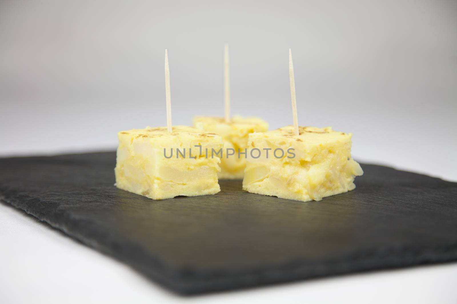 little portions with toothpick of yellow spanish potato omelette on black slate tray