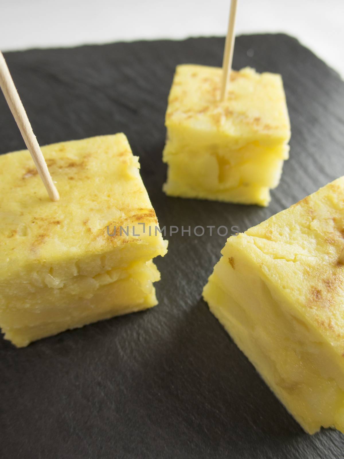 little portions with toothpick of yellow spanish potato omelette on black slate tray