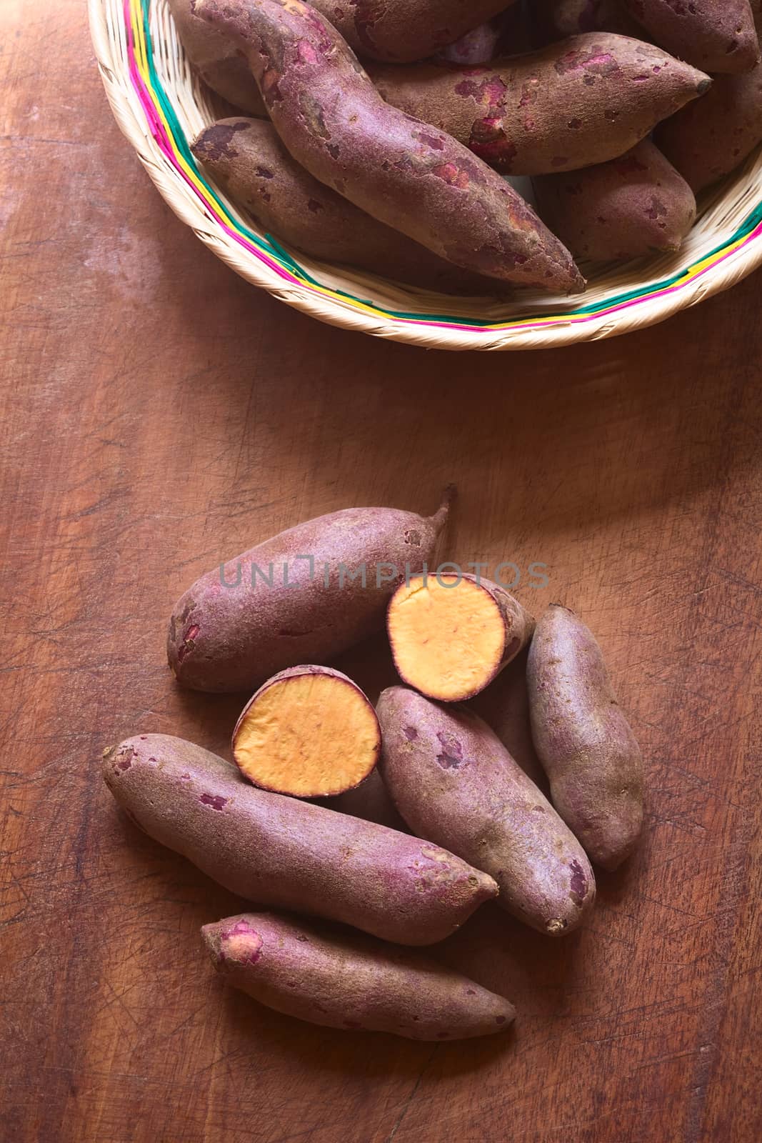 Overhead shot of raw purple sweet potato (lat. Ipomoea batatas) on wooden board photographed with natural light  