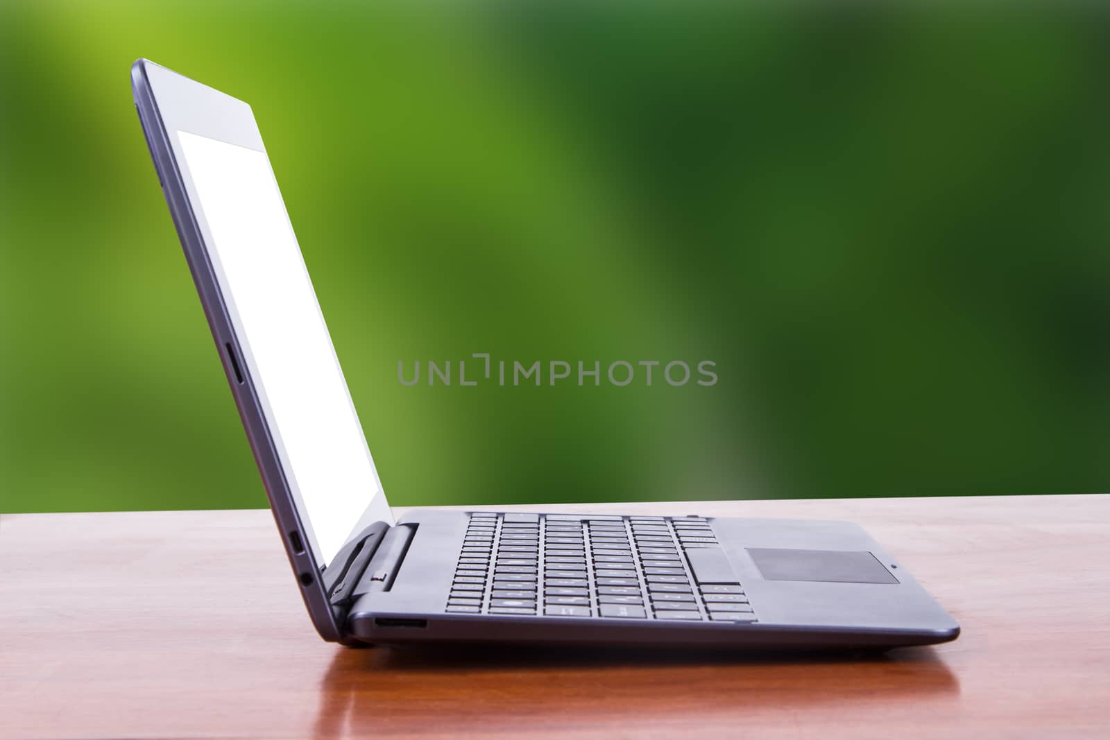 Tablet laptop with white blank screen on wooden table, side view, green natural background.