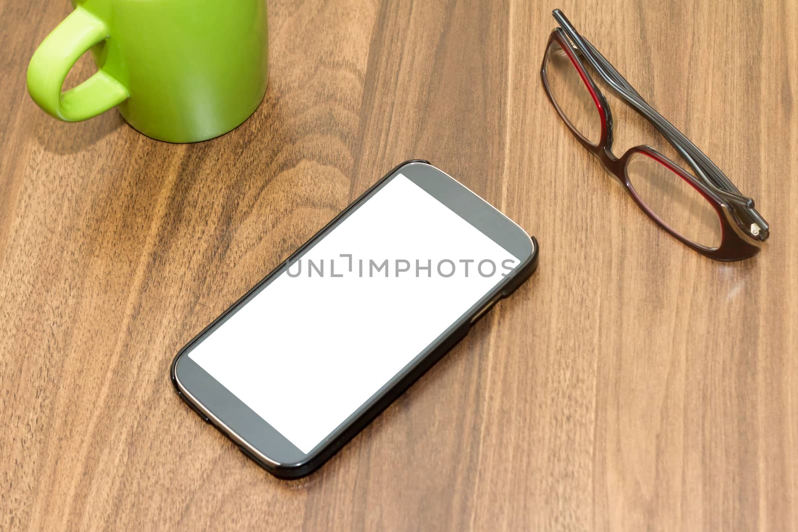 Top view of blank and white screen of smart phone with glasses and green cup on wooden table.