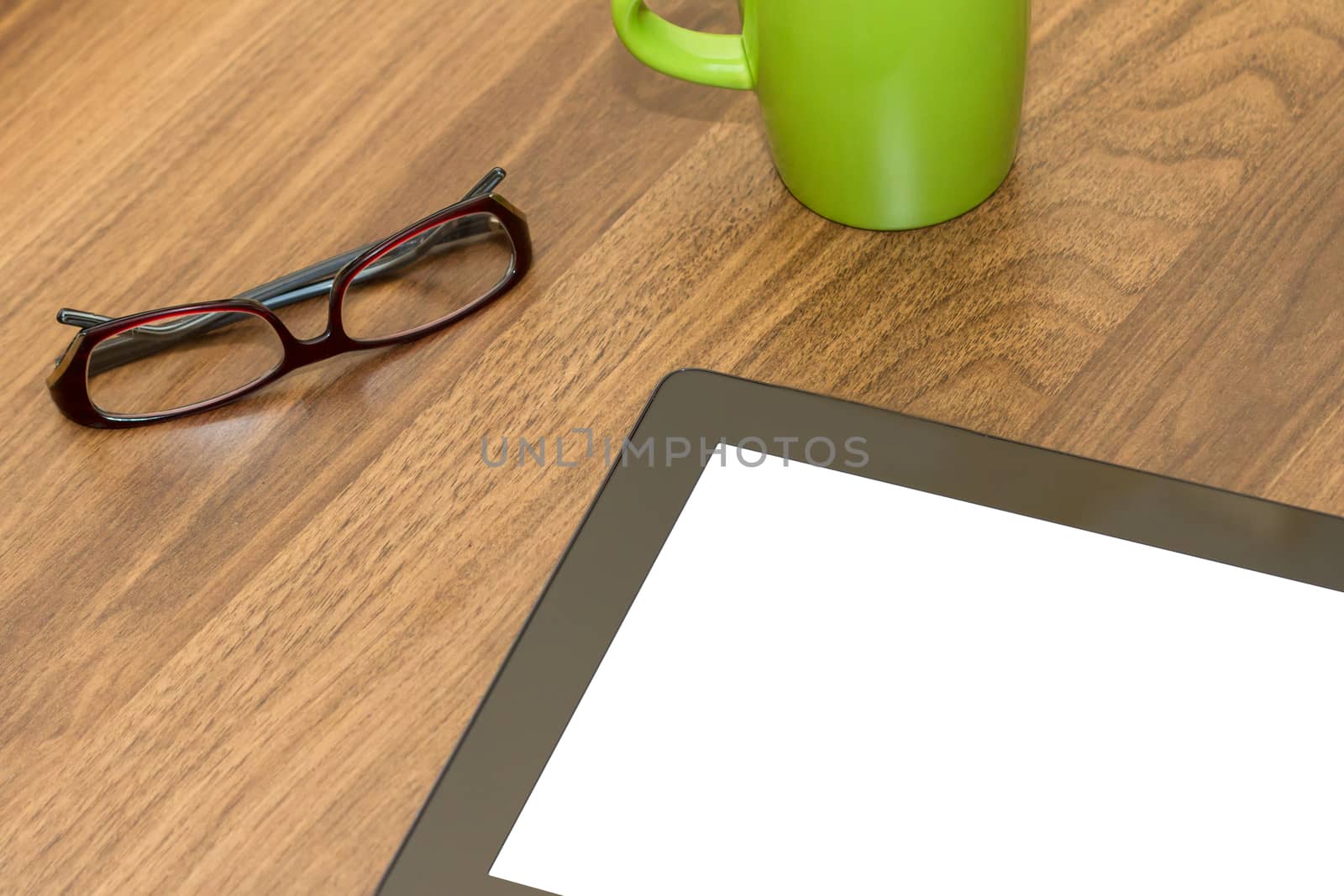 Top view of tablet with blank, white screen and coffee mug and glasses on wooden table.