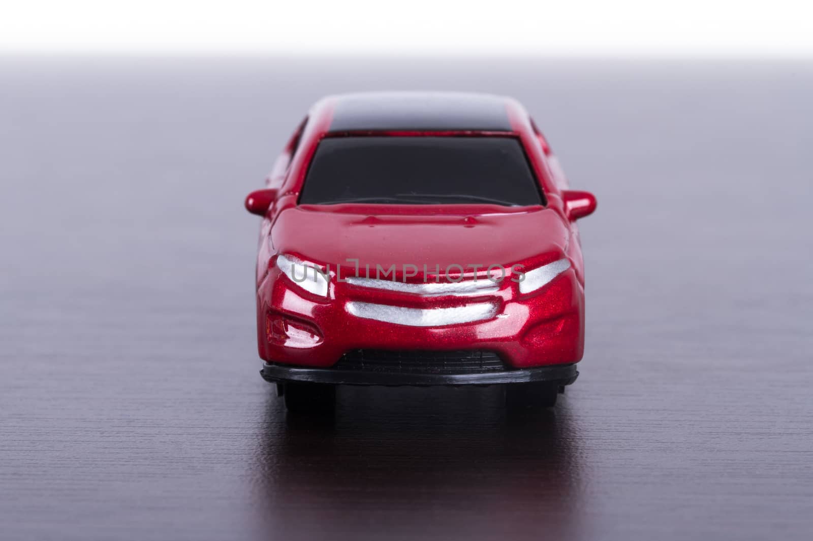 Front view of red, toy, small car on wooden table.