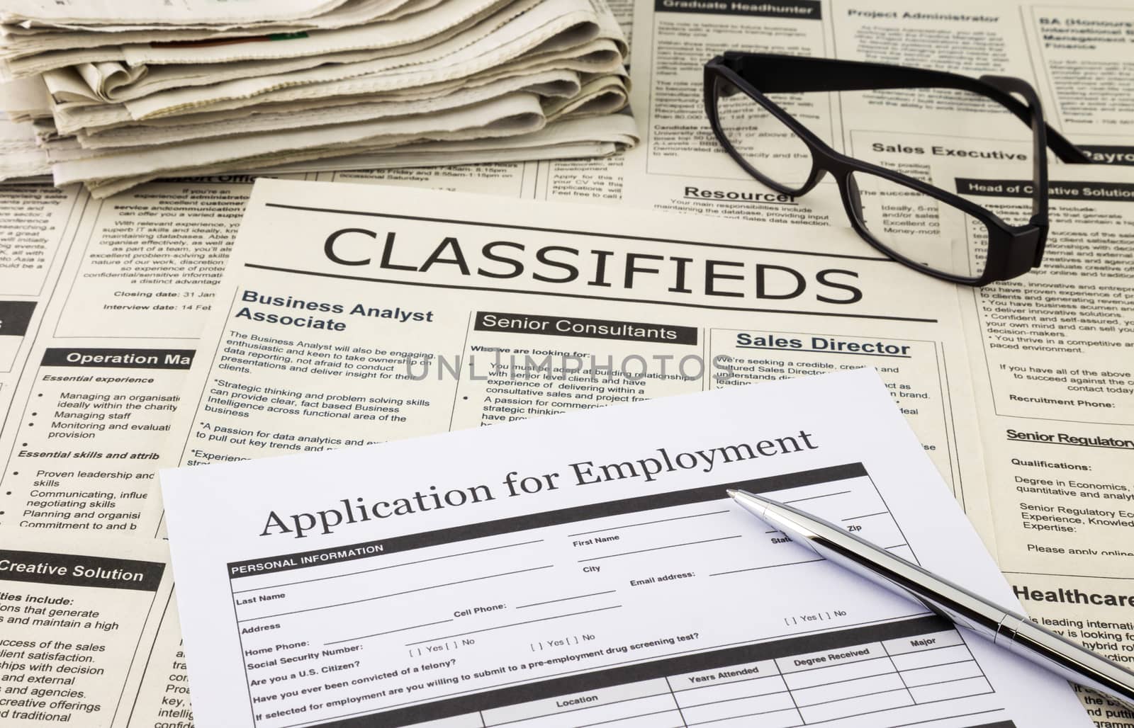 blank job application form place on fake classifieds ads with stack of newspaper and glasses