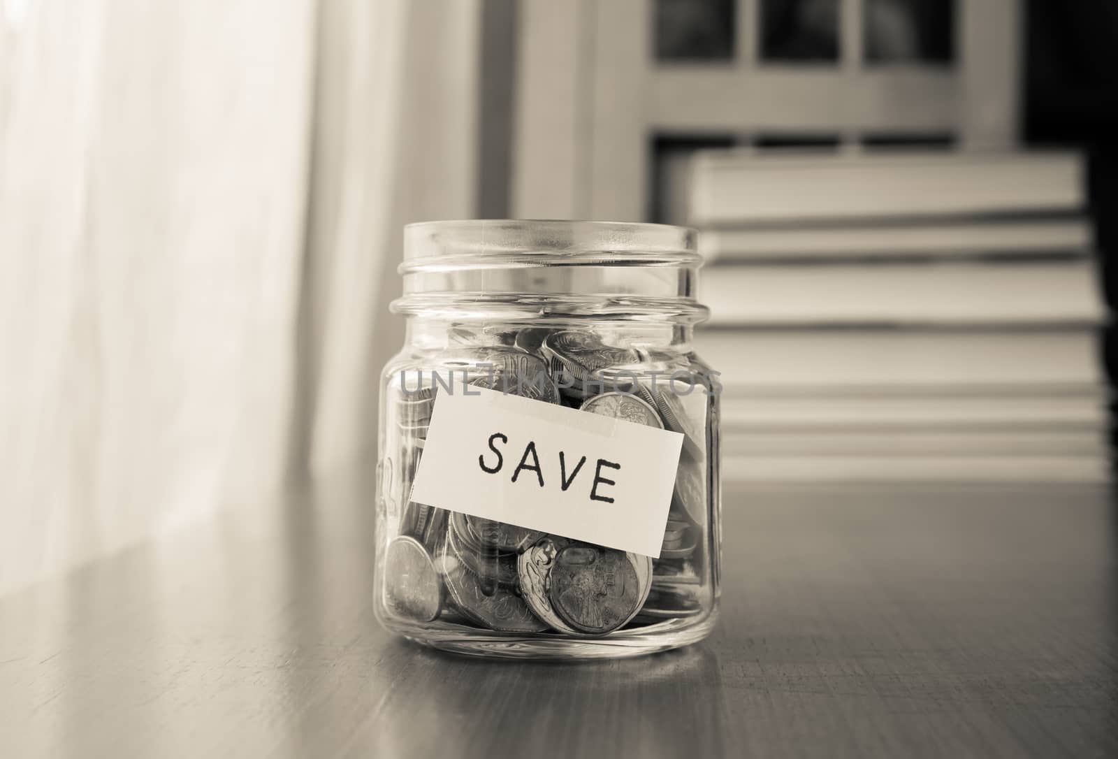 A savings money jar with world coins and save word on label or tag, black and white image