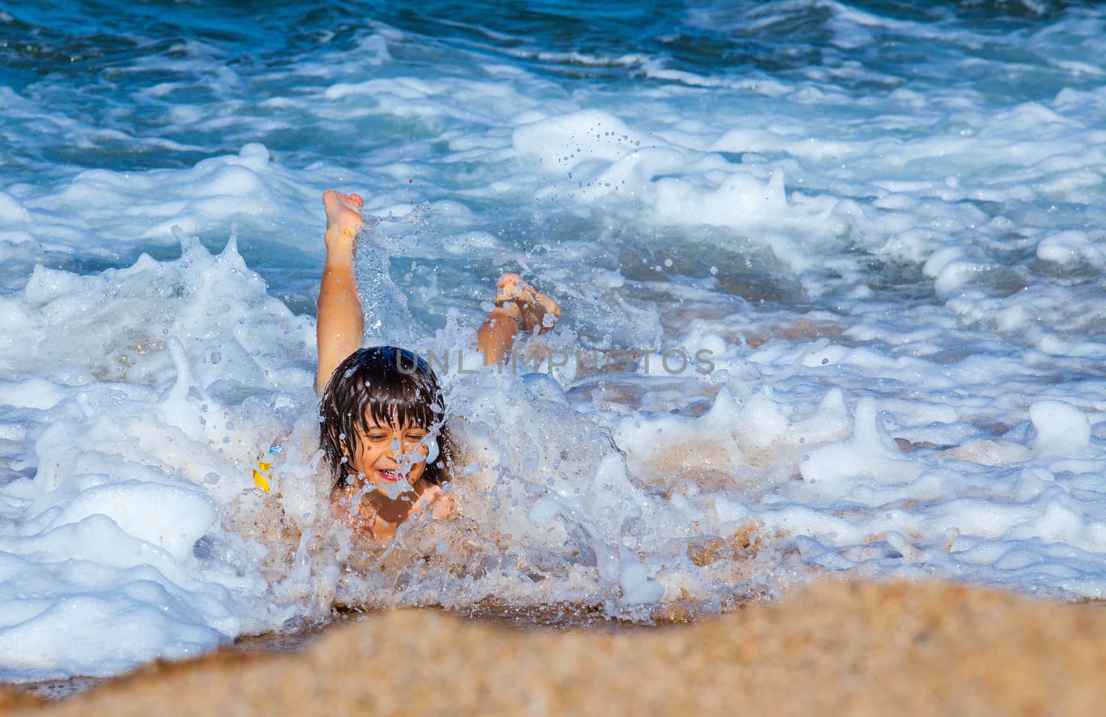 Little boy laughing in the foam of waves at sea by Astroid