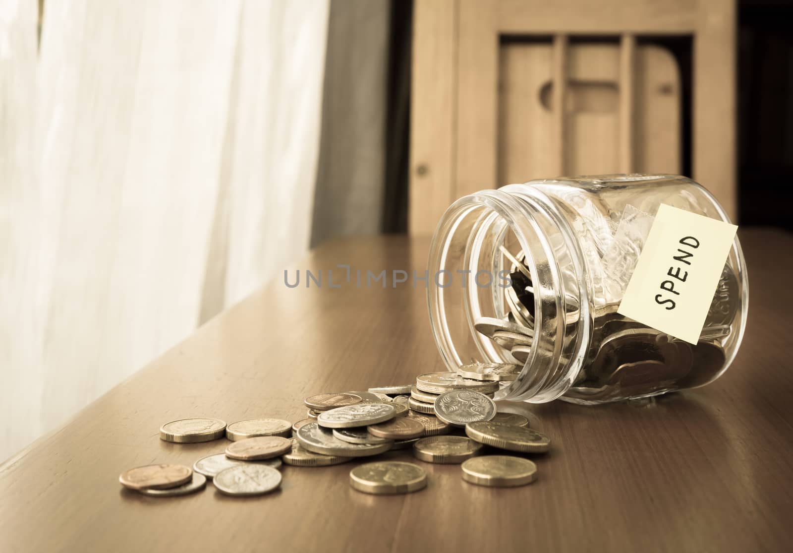 Many world coins spilling out of a money jar, spend word or label on jar