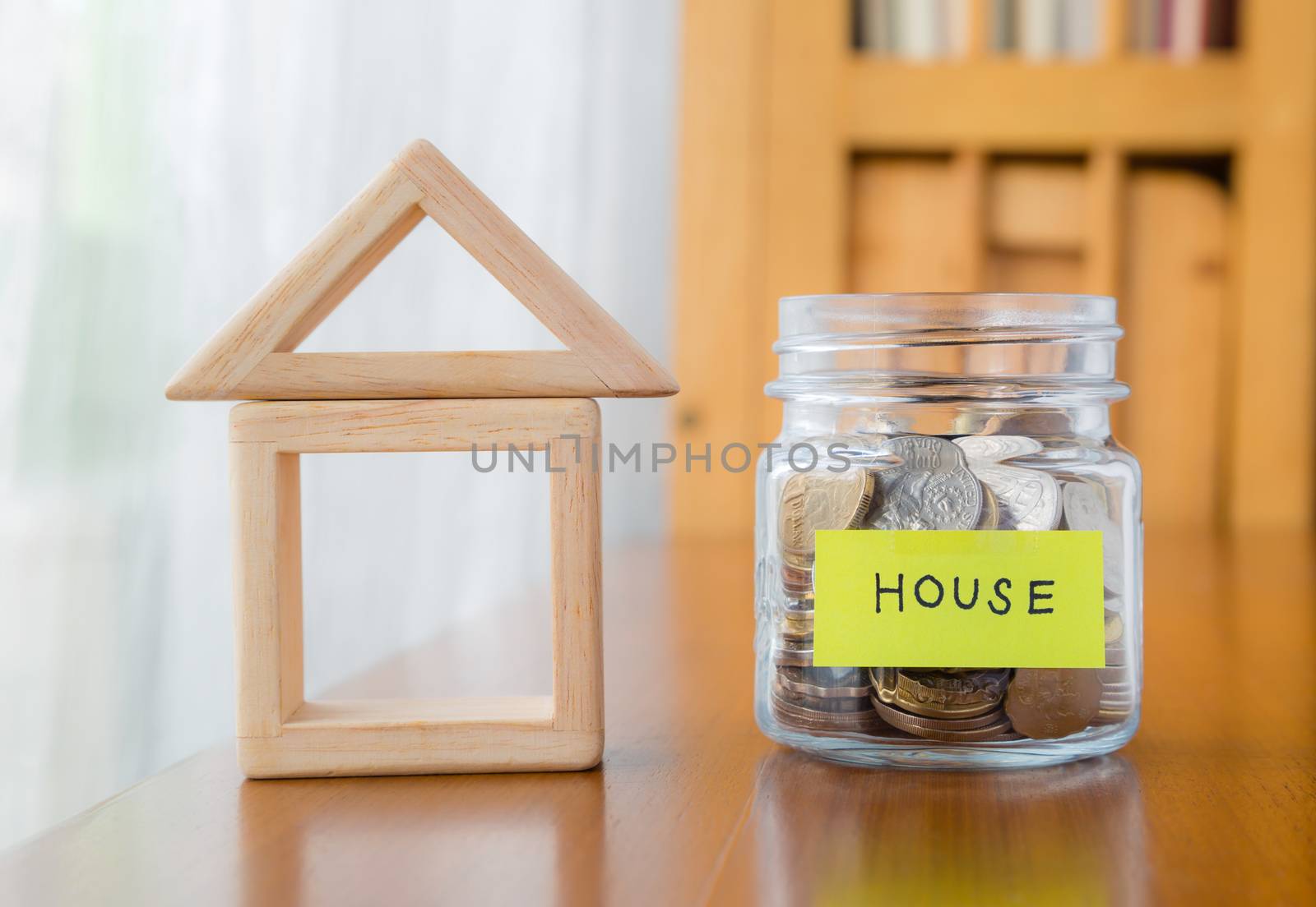 Glass bank with many world coins, house word or label on money jar and wooden home geometric blocks over table