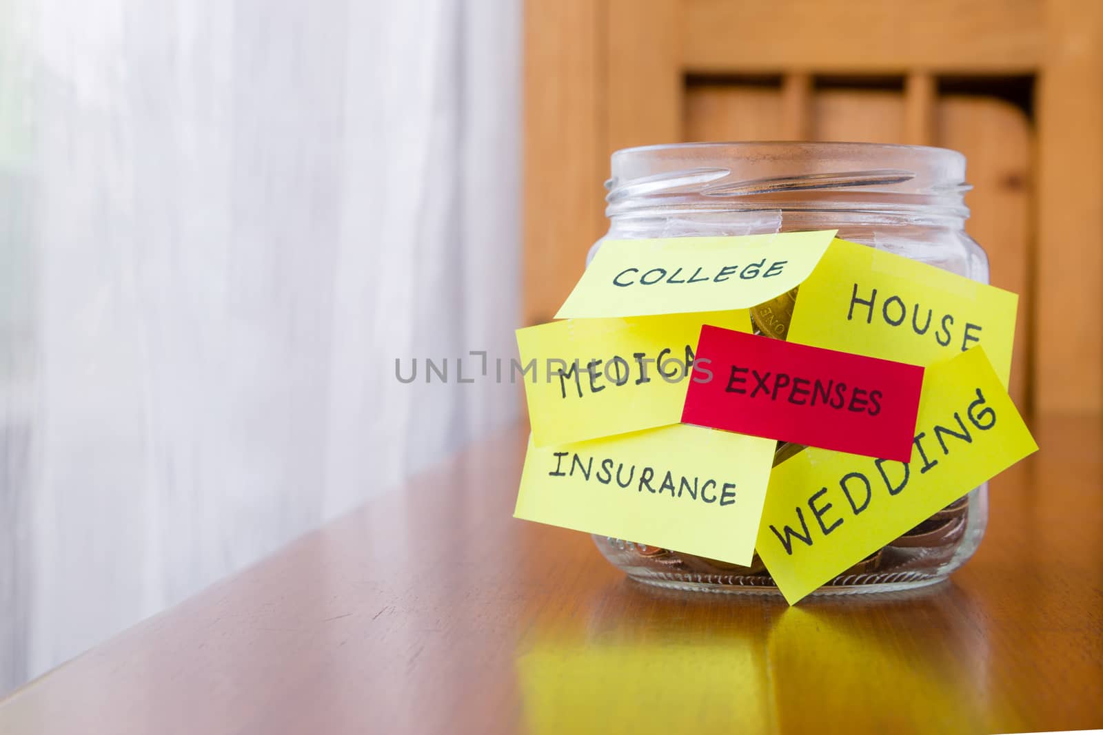 A jar of coins with expenses and other words or labels on savings money jar