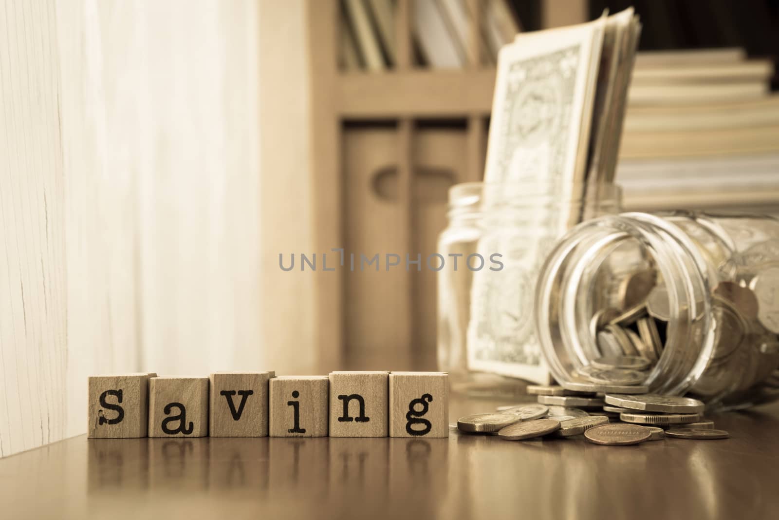 Saving word on rubber stamps place on table with coins and banknotes in money jars, sepia toning