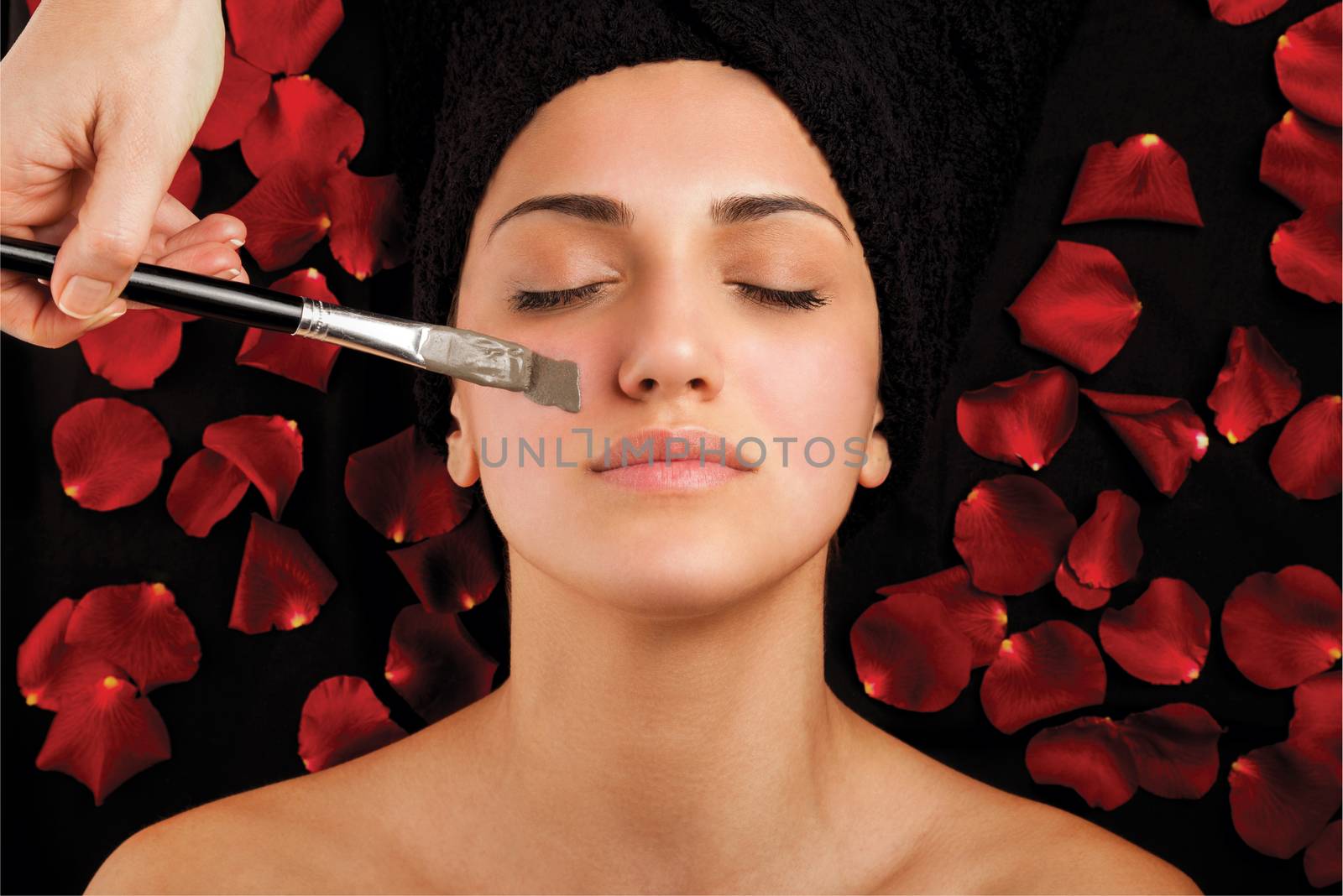 Woman during facial treatment with seaweed mask on bad with roses.