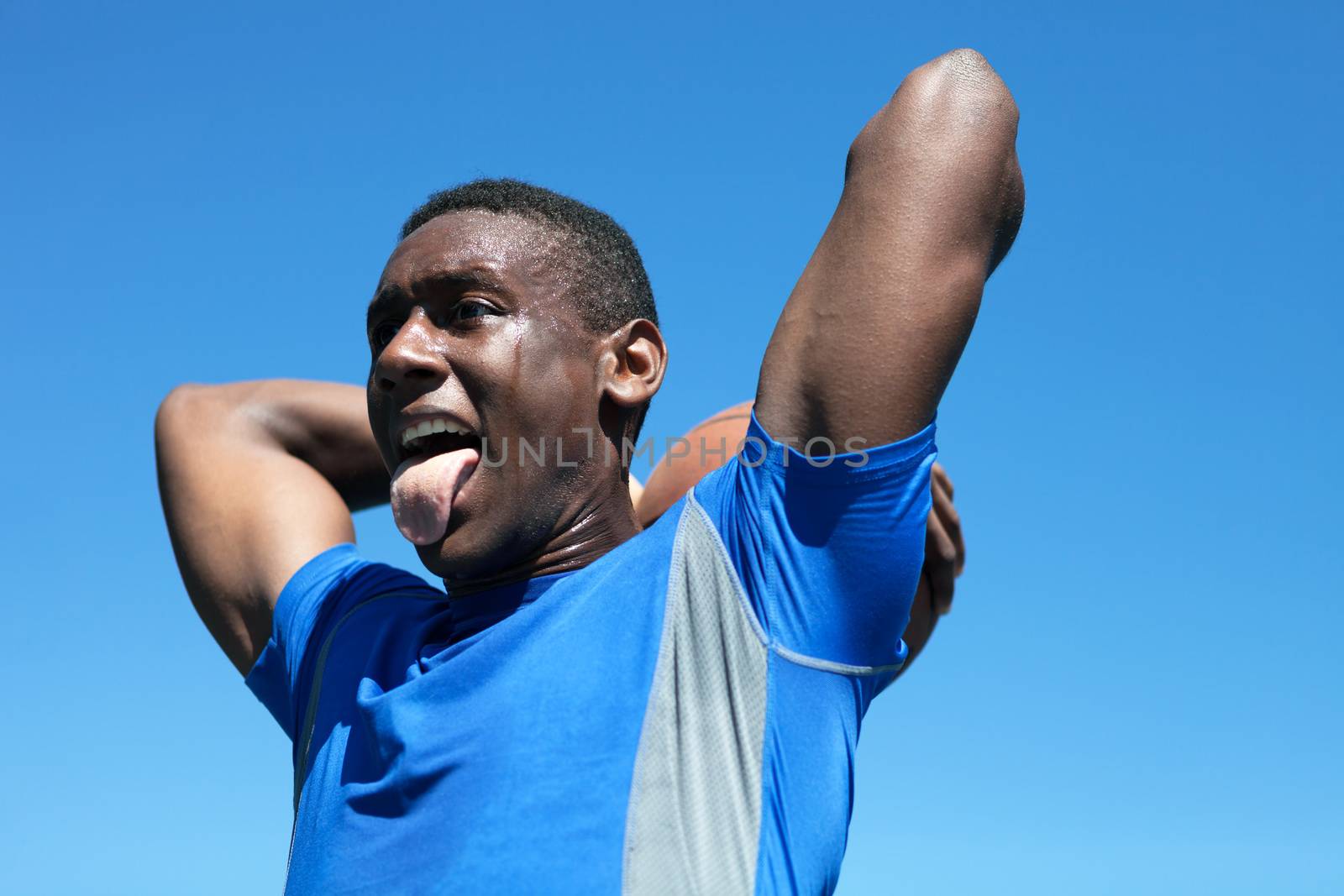 Young basketball player in his early twenties posing with the ball held behind his head.